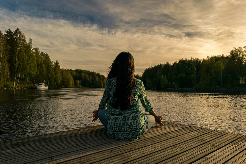 Woman sitting on a dock by lake meditating 