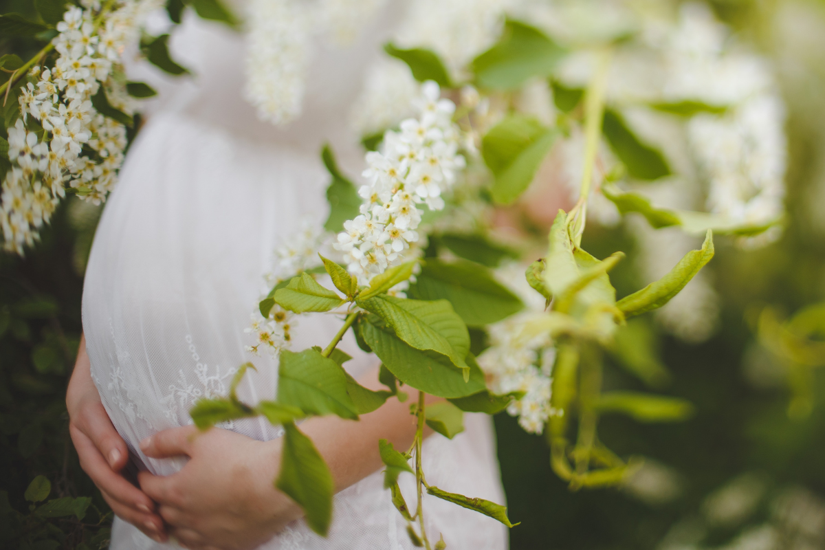 pregnant woman holding belly in white dress surrounded by flowers