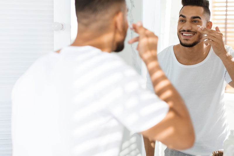 man looking at himself in the mirror about to apply skincare