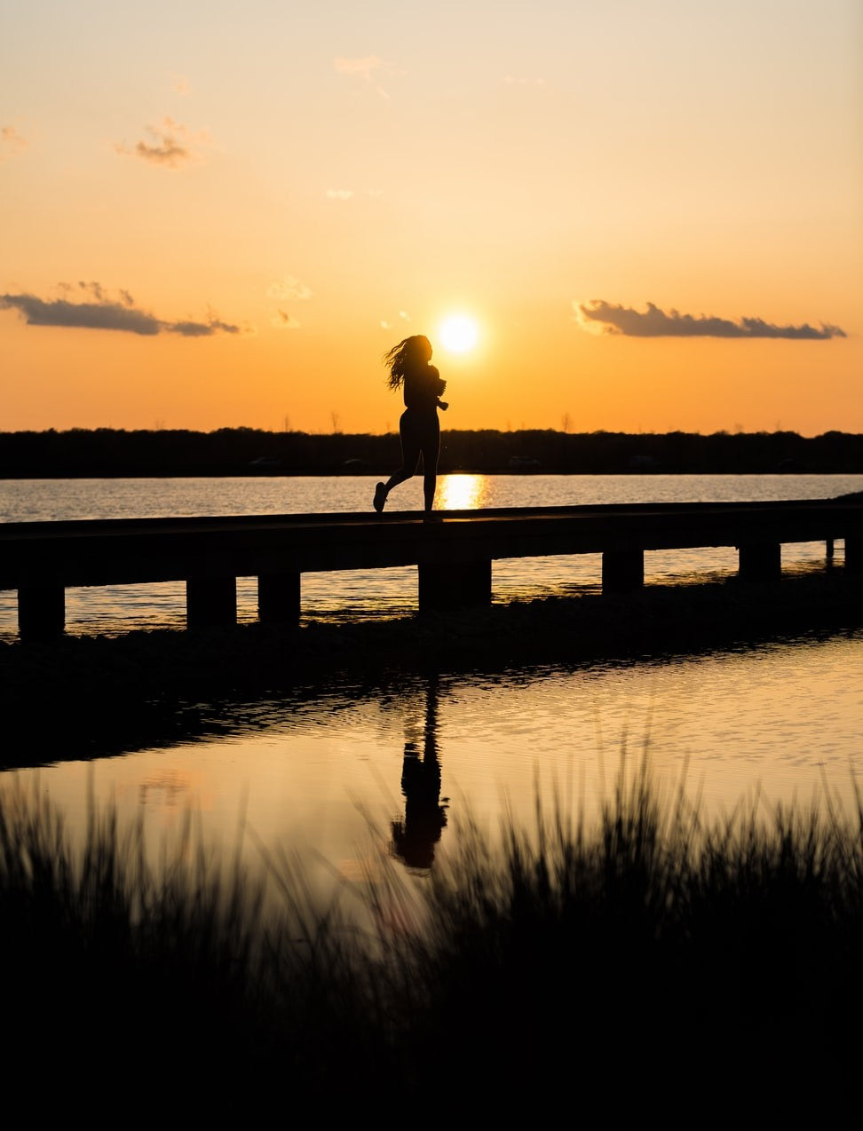 woman running along bridge with sunset in background