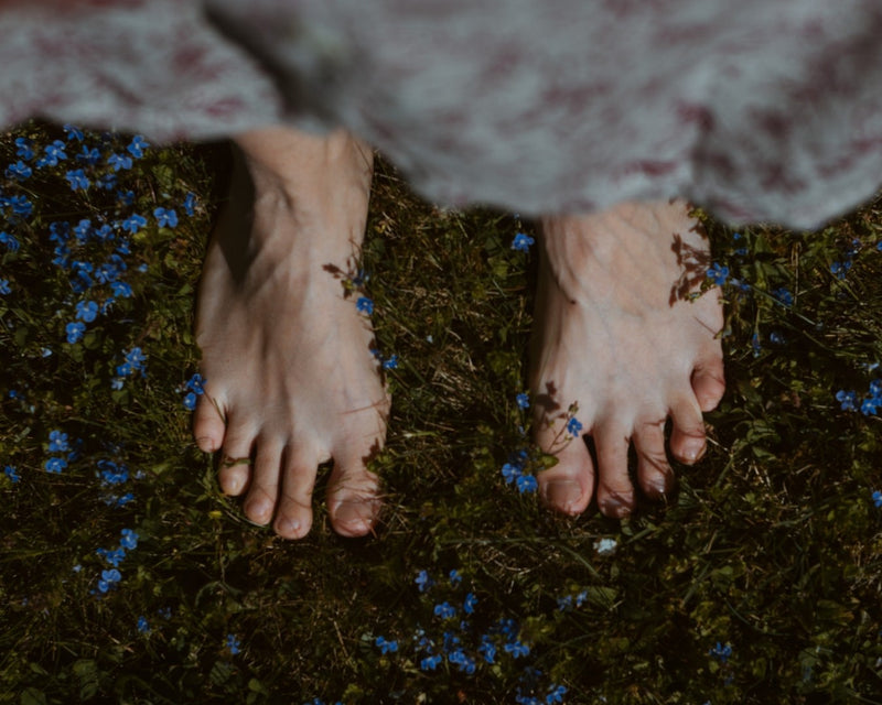 woman looking down at her feet which are surrounded by purple flowers