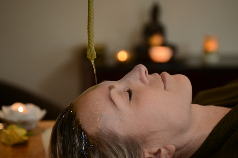 oil pouring onto clients head as she receives ancient shirodhara treatment for mental clarity and nervous system health